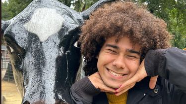 young man smiling with closed eyes next to the head of cow statue