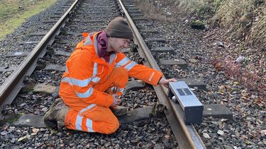 Man on a railway track holding device on the rails in front of bridge
