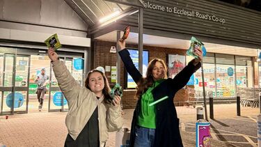 Two sheffield alumni jumping holding crisps outside of the coop shop 