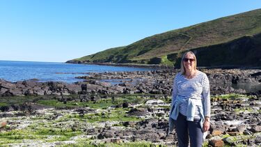 A photo of Maria Shemmens, University of Sheffield apprentice. She is standing at a rocky UK coastline on a sunny day looking straight at the camera.