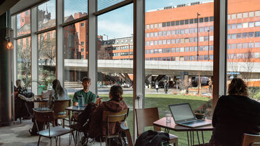 This image shows people sitting in a cafe with campus buildings in the background.