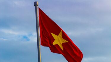 The flag of Vietnam against a blue sky with clouds
