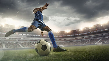 A man about to kick a football across the pitch.