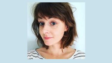 Kate smiling in front of a pale blue background