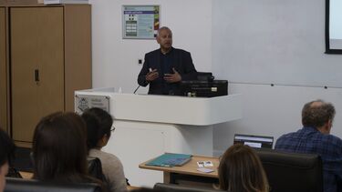Kamal Birdi speaking to a group of people in a lecture theatre.