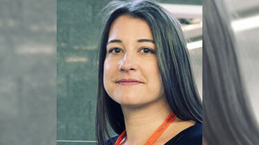 A headshot of Bella Abrams indoors, wearing a lanyard