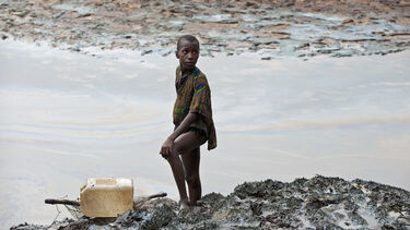 Child standing at oil polluted river bank in Goi