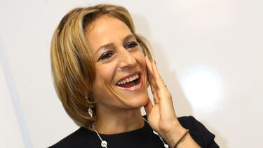 Emily Maitlis laughing in a black top against a white wall