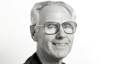 black-and-white headshot of Jack Barrott in his 60s, smiling and wearing glasses