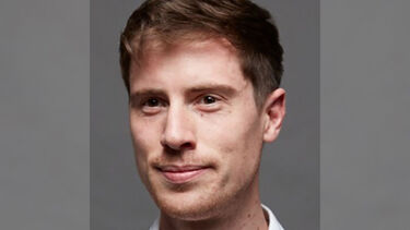 A headshot of Luke Impett smiling against a grey background