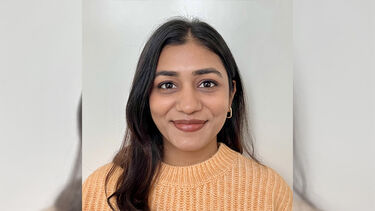 A headshot of Nikita Bansal smiling in an pale orange knitted jumper