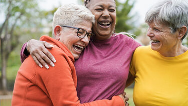 Three laughing middle-aged women with their arms around each other