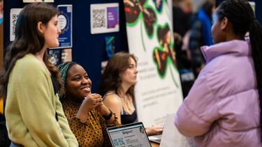 Students smiling and giving advice at a stand at a fair