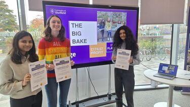3 women standing with certificates in front of screen celebrating competition success