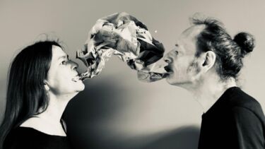 Two people connected by a cloth held in their mouths