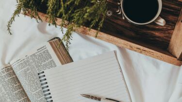 A book, a notebook and a mug on a white bed sheet 