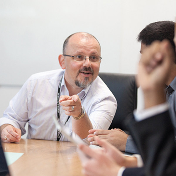 Profile picture of A photograph of Paul Latreille speaking to 2 students sat a table.
