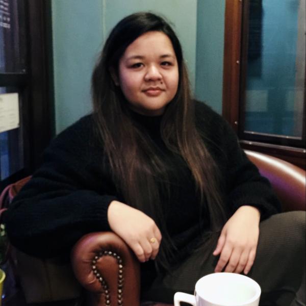 Profile picture of A photograph of Fasha Johanis sat on a leather armchair. On the table in front of her is a white mug.