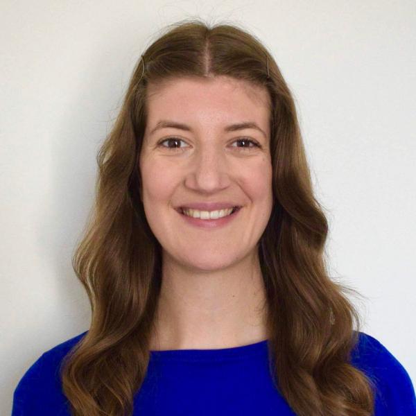 Profile picture of A woman with long brown hair is smiling at the camera. She is wearing a bright blue shirt.