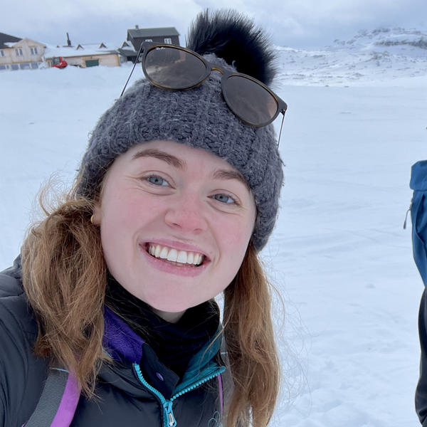 Profile picture of Charlotte Curry in a wooly hat, smiling in front of some snow