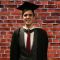 Graduate in cap and gown stands against wall