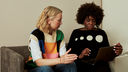 Photo of two women on a sofa, looking at a laptop