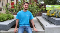 Dario Trimarchi in blue University of Sheffield student ambassador t shirt, sitting outside HRI building and smiling at camera