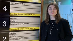 academic visitor from Ukraine Vira Dutkanych leaning against a bord indicating what is on which floor in Jessop West