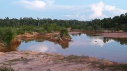 Water filled hole caused by mining surrounded by forest trees