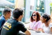 Four students laughing while sat at a bench, outside the Students' Union