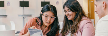 Three students sat at a table looking at a shared laptop screen