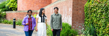 Three smiling students walk outside a red-brick building (Firth Court)