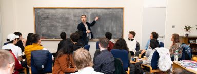 A lecturer stood at the front of a seminar by a blackboard
