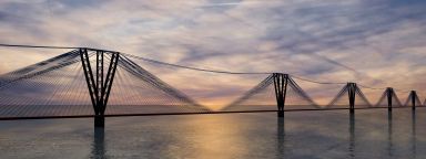 Image of long bridge over river at sunset