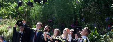 Group of happy graduating students throwing caps in air in summer