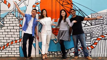 Four international students strike fun poses in front of mural 