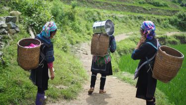 photo of three women carrying baskets on a hill path