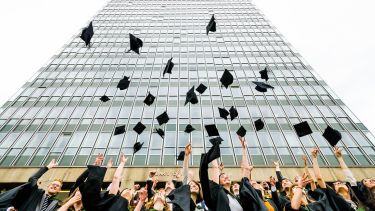 Graduates throwing hats outside Arts Tower