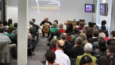 Cellist performing and talking at a seminar