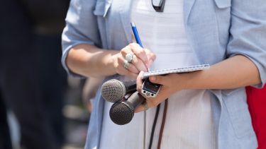 A journalist is taking notes while holding microphones