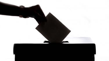 A person dropping a ballot paper into a box.