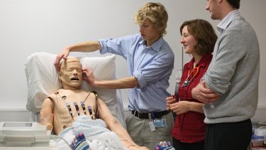 A group of medical students observing a demonstration on a dummy.