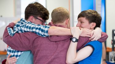 An image of three students in a group hug