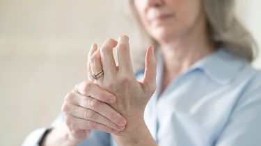 A photograph of a woman experiencing joint pain in her hands as a result of osteoarthritis.