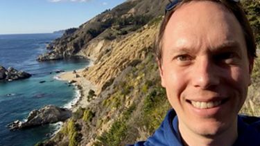 Dr Tom Darton on top of a cliff with water in the background. 