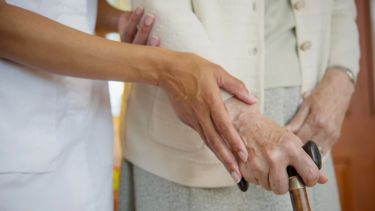 A medical practitioner assists an elderly person who is using a walking stick