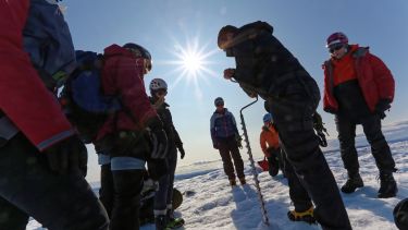 Researchers drill into ice while the sun beats down on them