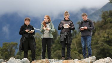 Four students study their notes during fieldwork in New Zealand