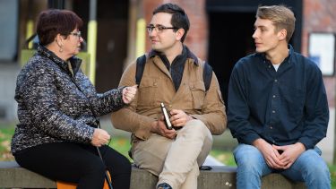 Two students sitting on a bench talking to a Sheffield resident