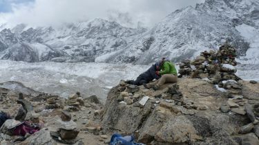 Two researchers sat on rock in front of snow mountains